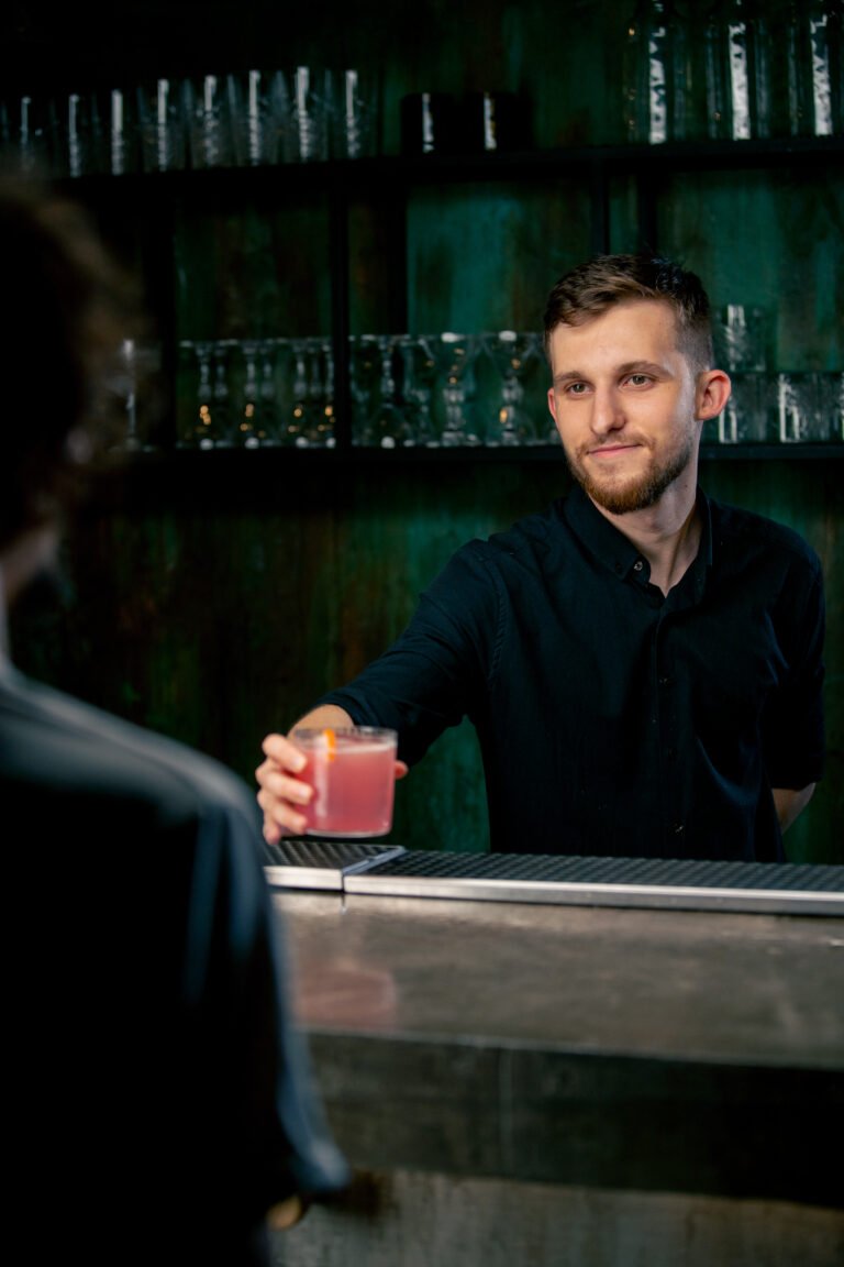 Bartender holding a glass filled with fresh rose cocktail with sour and sweet taste give it client