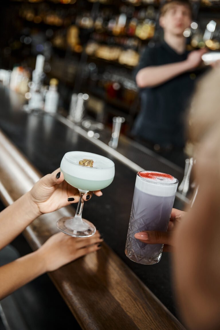 cropped view of multiethnic women holding delicious cocktails while spending time in bar after work